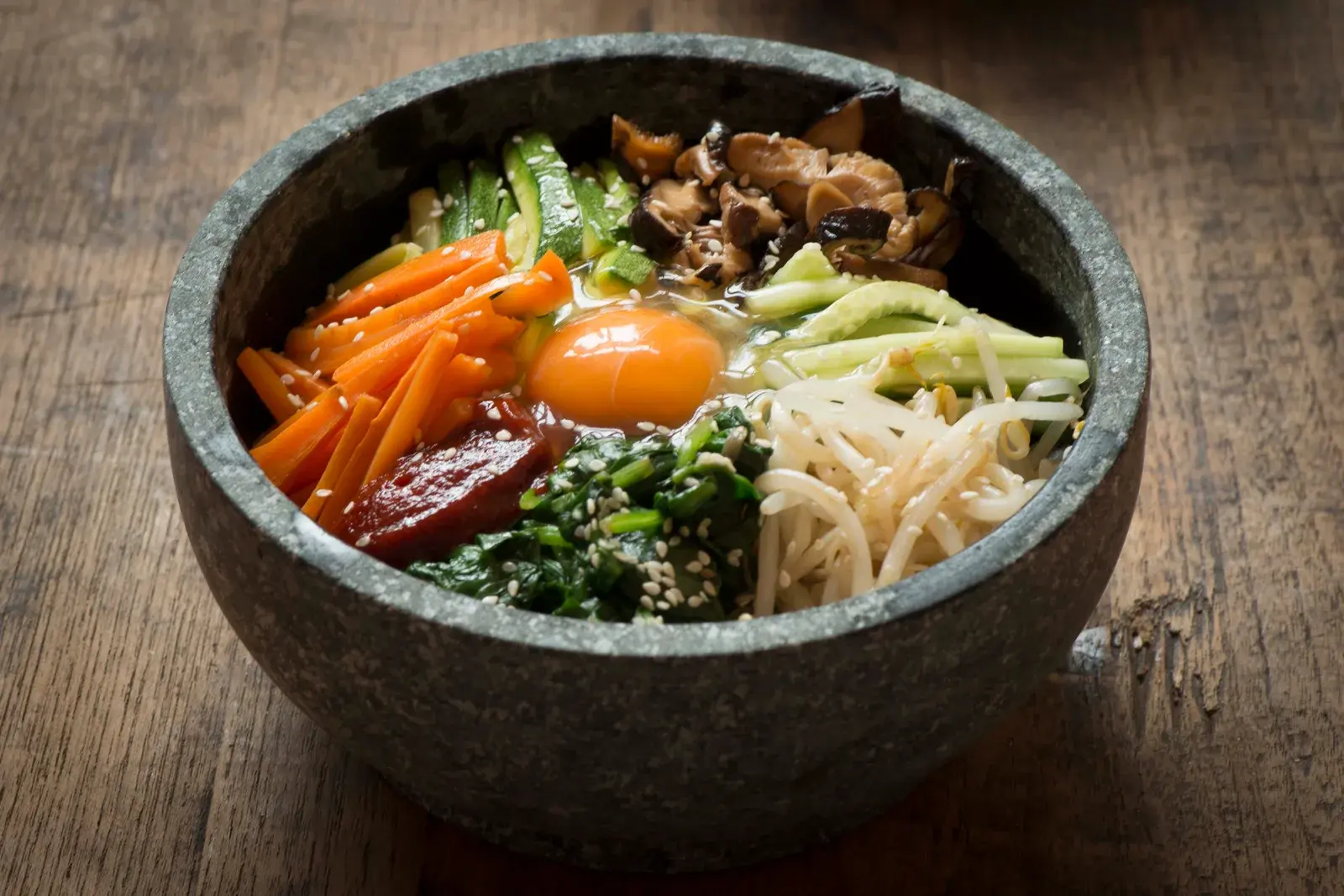 Bibimbap mixed rice bowl with vegetables and meat in a hot stone bowl