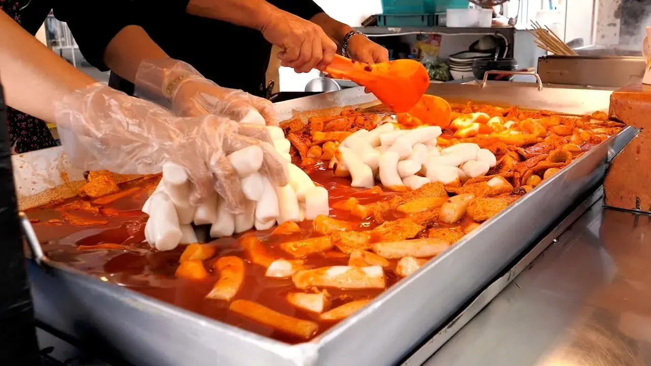 Street vendor cooking spicy tteokbokki rice cakes in a pan